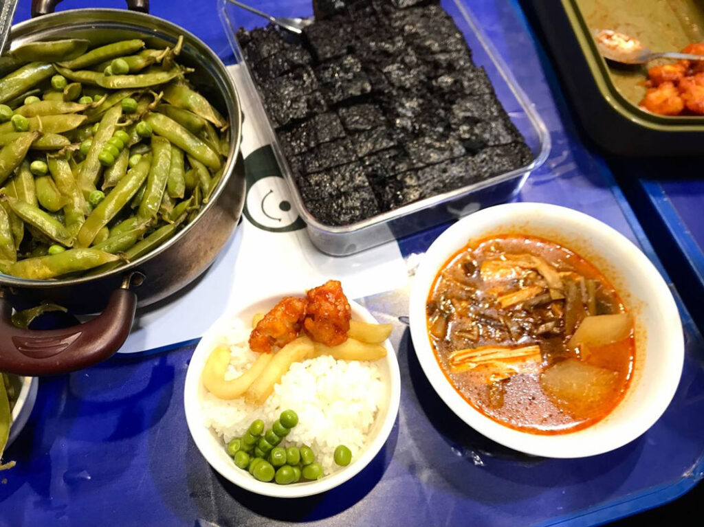 파란색 간이 탁자 위에 통과 냄비에 담긴 여러 음식, 그릇에 담은 음식 등이 놓여있다.